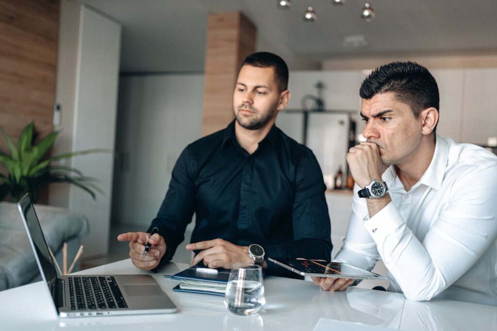 Two men in office attire focused on laptop, discussing business strategies.